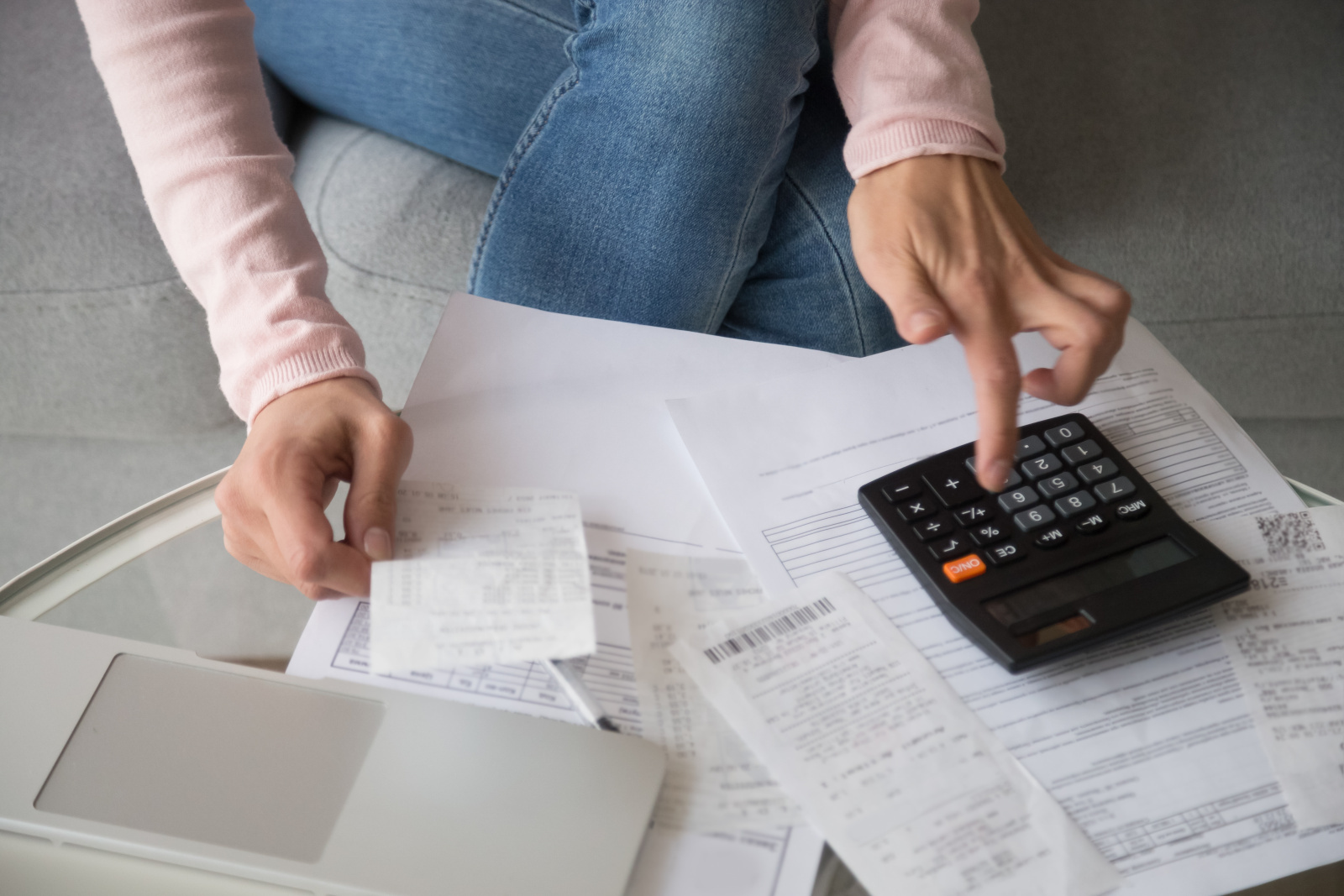 Žena držiaca v ruke účtenku pri počítaní na kalkulačke.
